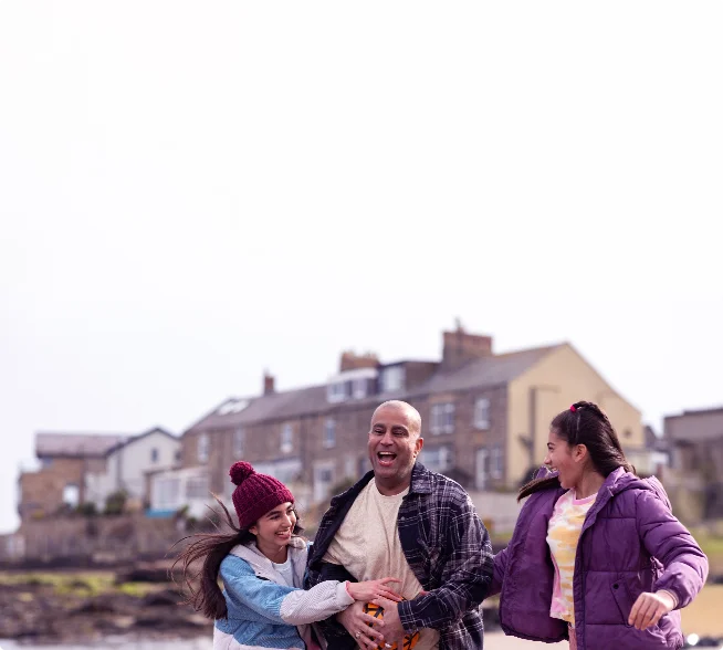 Family smiling and playing together on a sandy beach near the water.